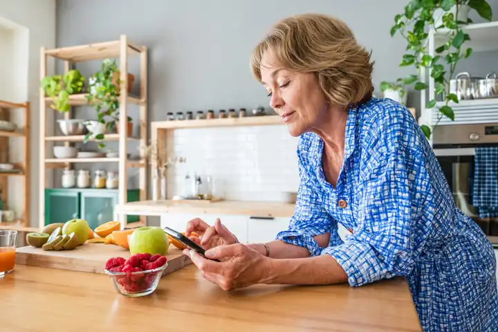 Moteris virtuvėje prie vaisių skaito žinutę telefone